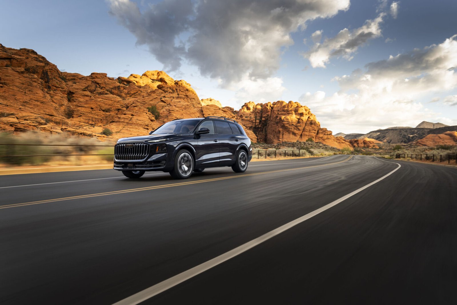 Audi Q9 negro circulando por una carretera entre formaciones rocosas
